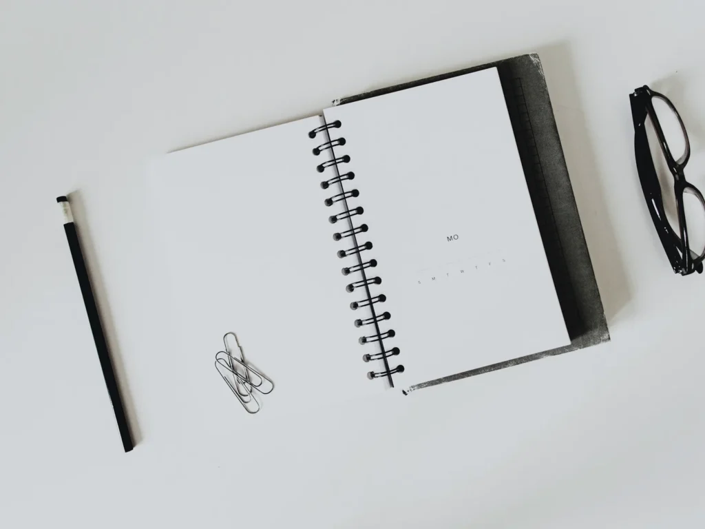 Quaderno a spirale, matita e occhiali su una scrivania chiara: scrivere un piano marketing